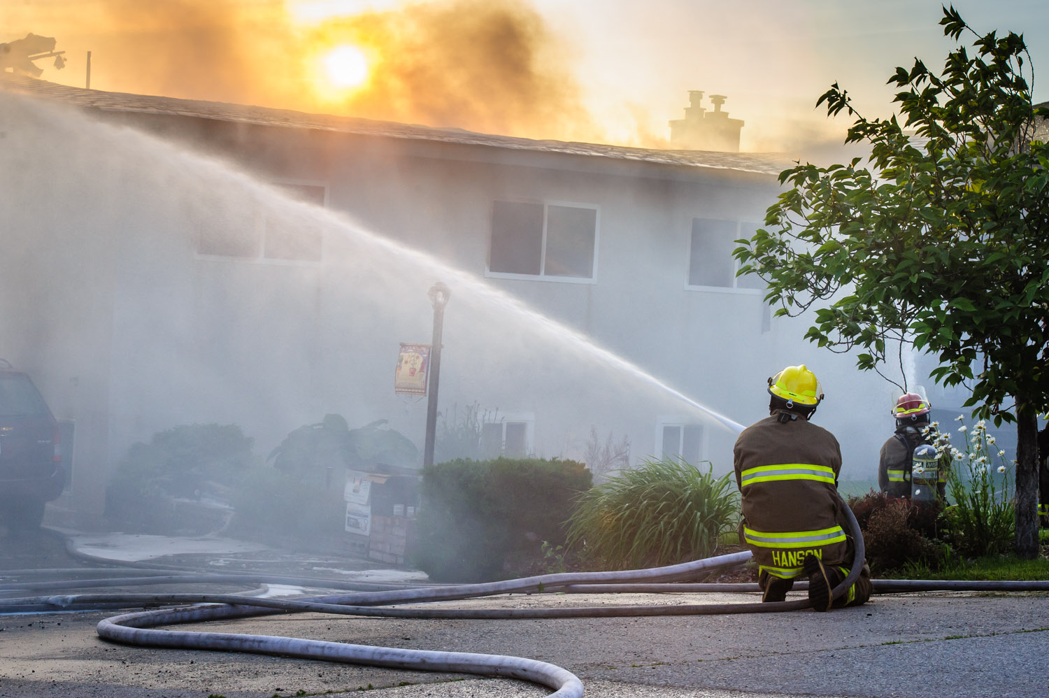 Osoyoos firefighter Chris Hanson hoses down a house on 33rd Street to try to contain the blaze. The evening sun looks eerie through the black smoke. (Richard McGuire photo)