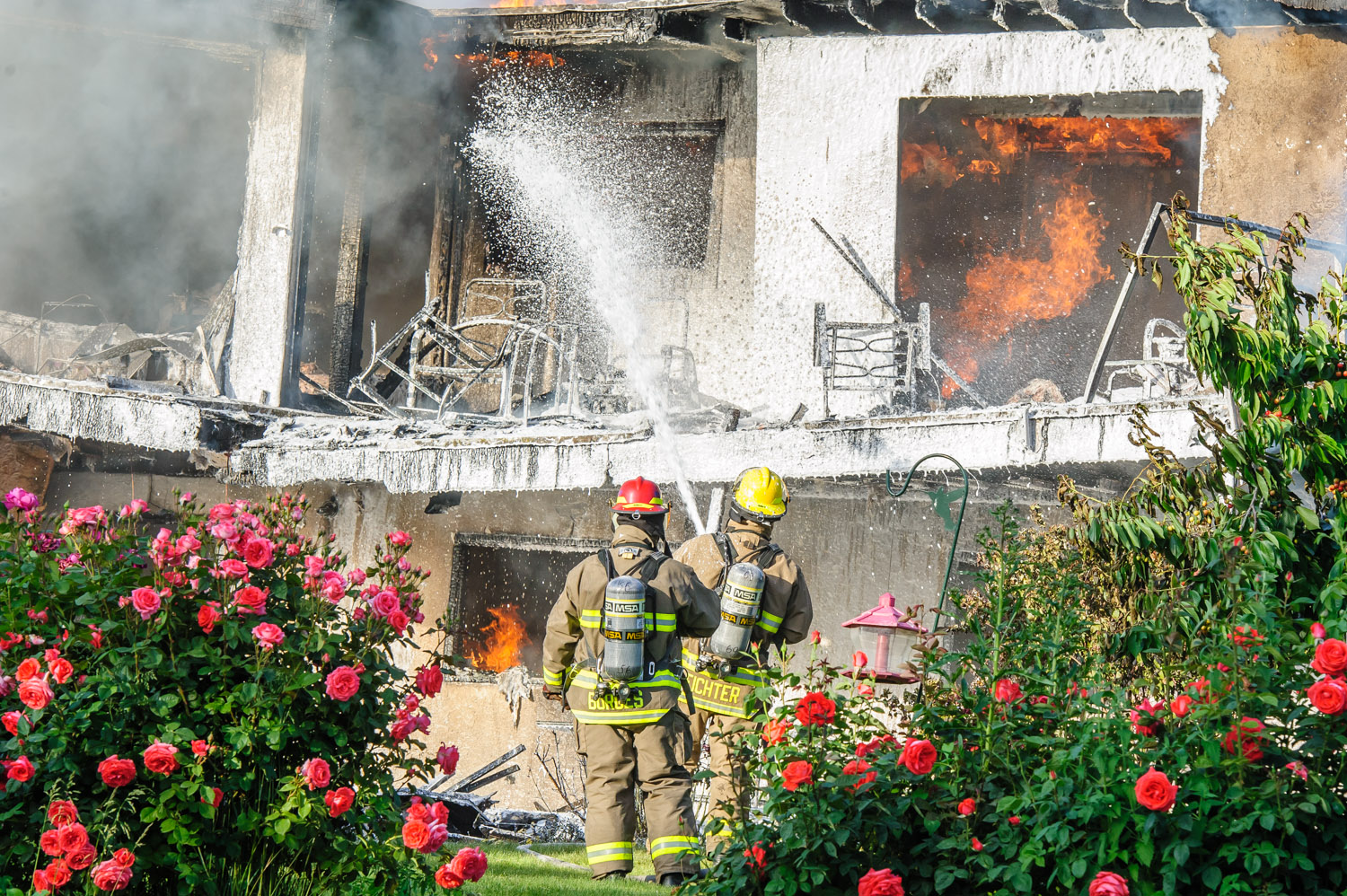 Osoyoos firefighters spray water and foam onto a 33rd Street house from the back rose garden to try to contain the fire in a strong breeze. (Richard McGuire photo)