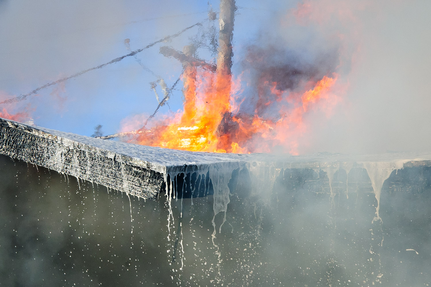 Flames leap from the roof of a burning house while water and foam sprayed by firefighters trickles off the collapsing rooftop. (Richard McGuire photo)