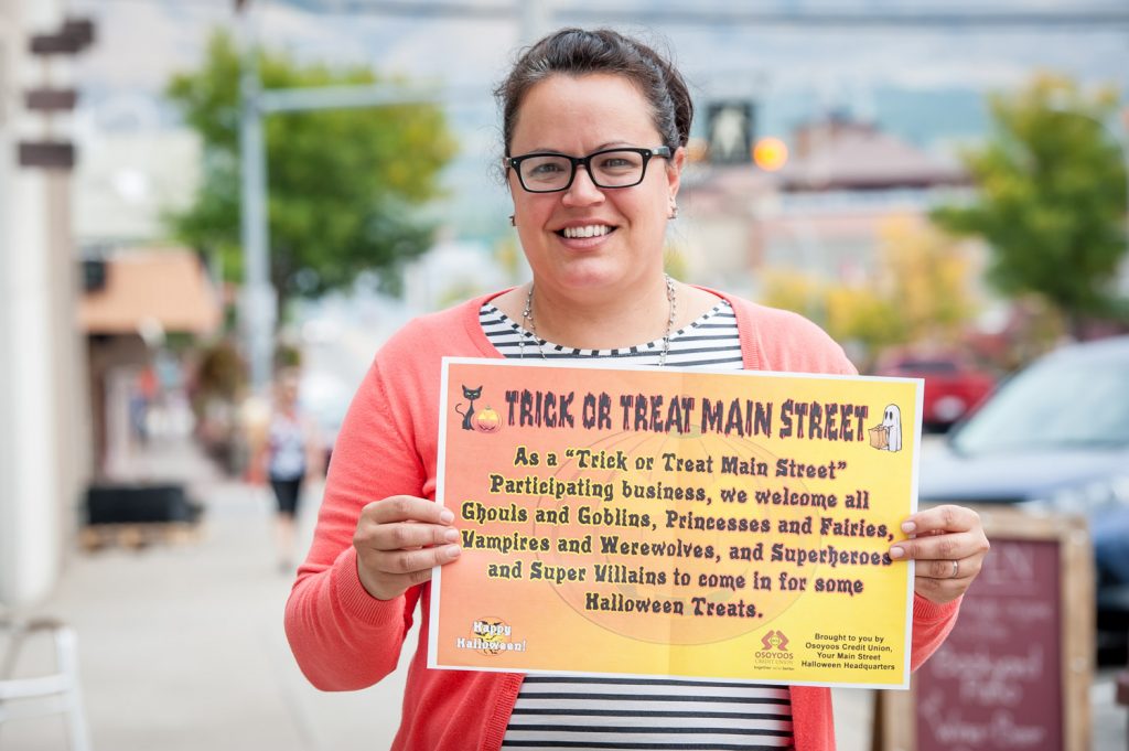 Halloween fan Michelle Quail of Osoyoos Credit Union shows the poster that businesses can put in their window on Halloween to welcome children to their stores. (Richard McGuire photo)