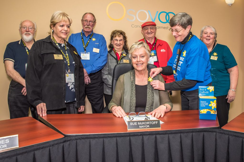 Osoyoos Mayor Sue McKortoff (centre front) proclaimed April to be Daffodil Month in Osoyoos last week. Pinning a daffodil on her was Donna Kelso, secretary treasurer of the Kiwanis Club of Osoyoos. The month raises funds for the Canadian Cancer Society through the sale of daffolils as well as raising cancer awareness. This is the first year the local Kiwanis Club has taken on the project. From left behind the mayor are: Wayne Sargent, Angelica Bachynski, Dick Mayer, Marjorie Dean, Bill Dean, Kelso and Allisen Sargent (club president). (Richard McGuire photo)