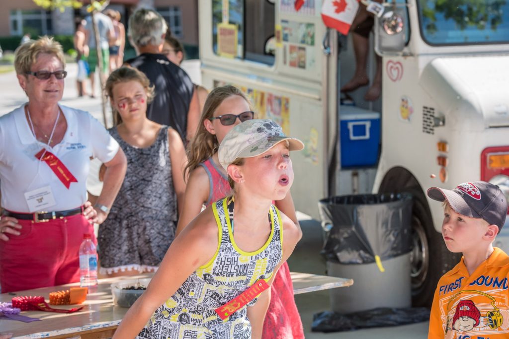 A young girl fires a cherry pit perilously close to a young boy's head during the cherry pit spit at Cherry Fiesta. (Richard McGuire photo)