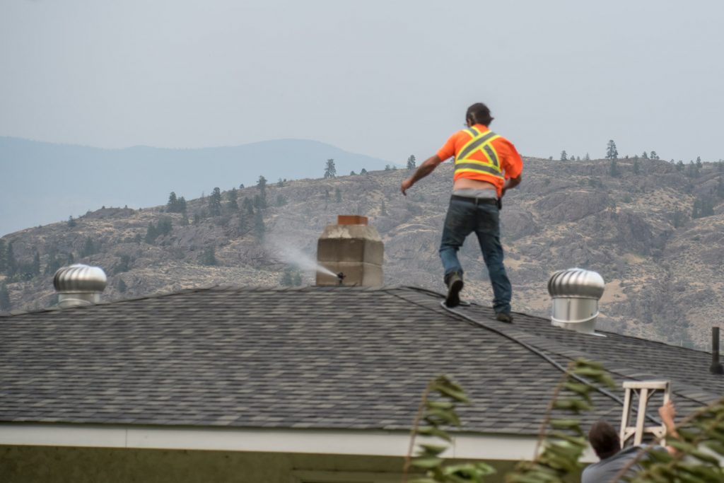 Men wet down the roof of a house on the east side of Highway 97 as a large fire approaches from the Testalinden Creek. (Richard McGuire photo)