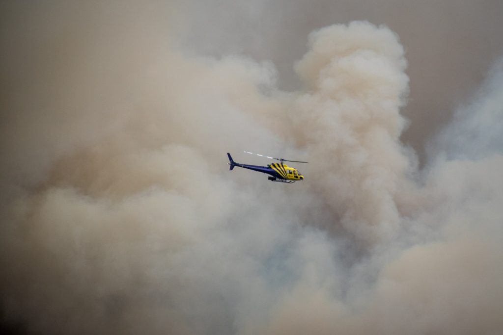 A helicopter flies through smoke and powerful winds by the Testalinden fire north of Osoyoos. B.C. Wildfire Service resources are spread thin with numerous fires in the area. This photo was taken at 6:48 p.m. Friday. (Richard McGuire photo)