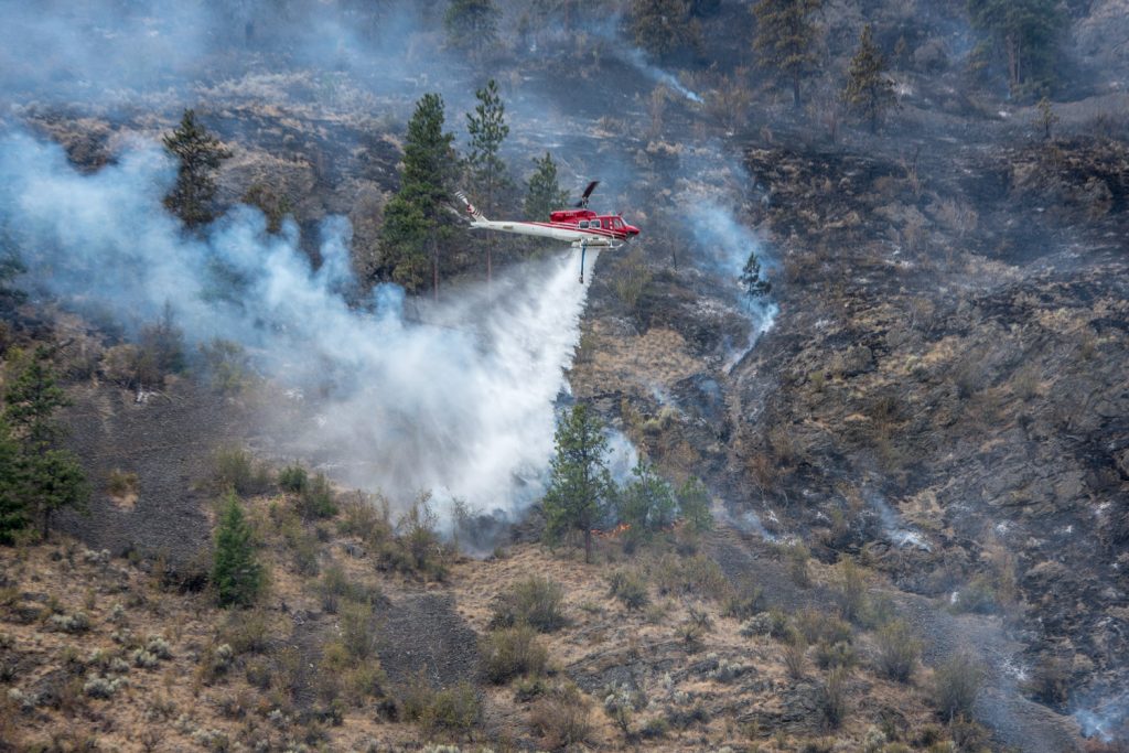 A helicopter drops water from a nearby slough onto the Testalinden Creek fire near Road 20 and Highway 97 just after noon Saturday. (Richard McGuire photo)