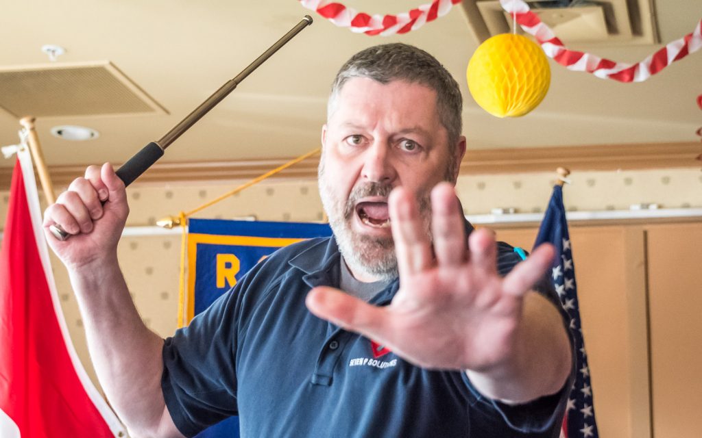 Marcus Alden, a recent guest speaker at the Rotary Club of Osoyoos, yells at a reporter to "Get back!" as he brandishes a collapsible baton. Alden was showing how a potential victim can turn the tables on a "bad guy" attacker. He warned the reporter ahead of time that he would be part of the demonstration. (Richard McGuire photo)