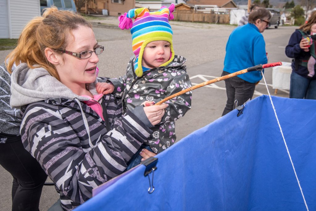 Little Izabel Mercer, 2, catches a fish while her mother Amanda Mercer holds up at the fish pond. Cathie Baskett played "fish ferry," putting age and gender appropriate "fish" on the end of the line. (Richard McGuire photo)