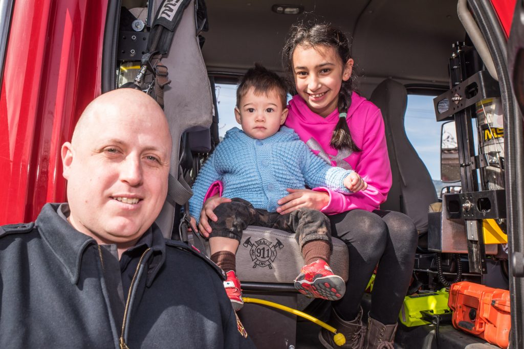 Adam Cebuliak, 1,and Vanessa Cebuliak, 11, of Richmond, tried out one of the fire trucks of the Osoyoos Volunteer Fire Department. Firefighter Casey Brouwer (left) helped them up. Brouwer had a head start for the head shaving event taking place next to them. (Richard McGuire photo)