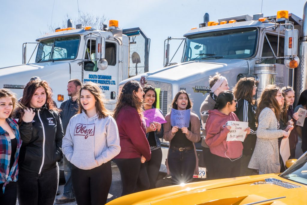 Students hold signs and show their support for OSS against a backdrop of concrete trucks. (Richard McGuire photo)