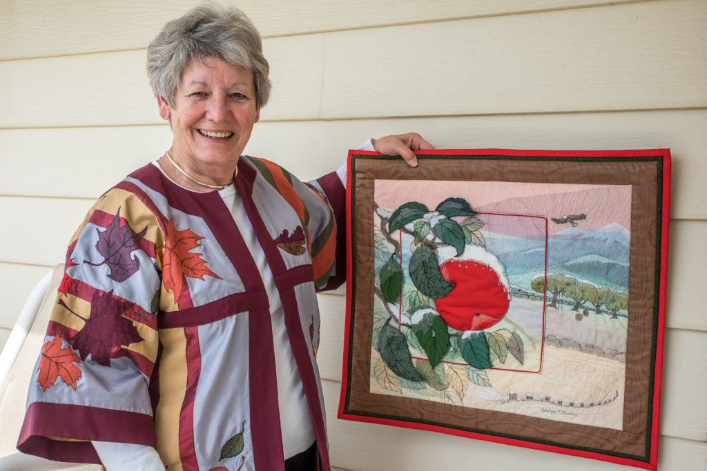 Osoyoos Art Gallery Curator Sue Whittaker shows one of the fabric art pieces done by Shirley Nilsson that will be shown in the exhibition opening Saturday, April 30. The clothing Whittaker is wearing was also designed by Nilsson. (Richard McGuire photo)