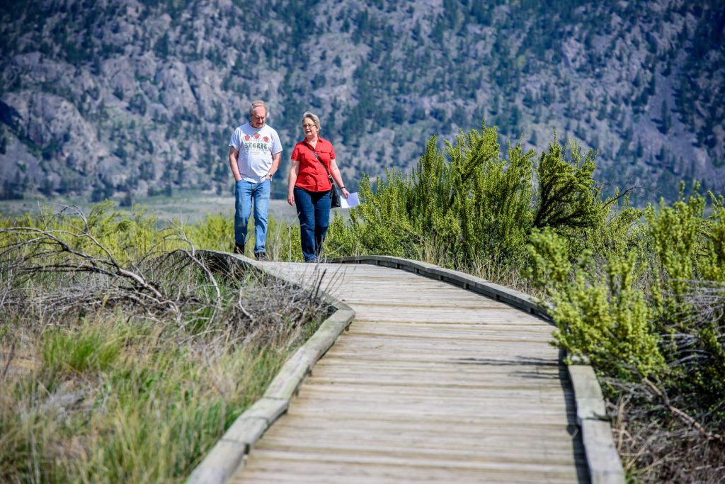 A man and woman walk along the boardwalk amid flowering antelope brusch at the Osoyoos Desert Centre. The centre opened for the season Saturday with an open house. (Richard McGuire photo)
