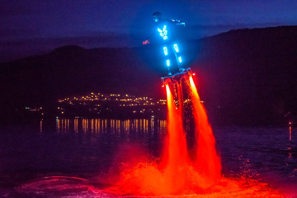 Curtis Pangrass flies and flips through the air propelled by powerful jets of water in the sport of flyboarding. For this demonstration Saturday night, he wore a suit with lights and the water jects were lit up with brilliant red lights. A member of Team Canfly, Pangrass, from Edmonton, did demonstrations on the weekend at Walnut Beach Resort. The event was arranged by Travis Blacklin, proprietor of Canadian Jet Pack Adventures, who is operating a flyboarding concession at the resort again this summer. (Richard McGuire photo)