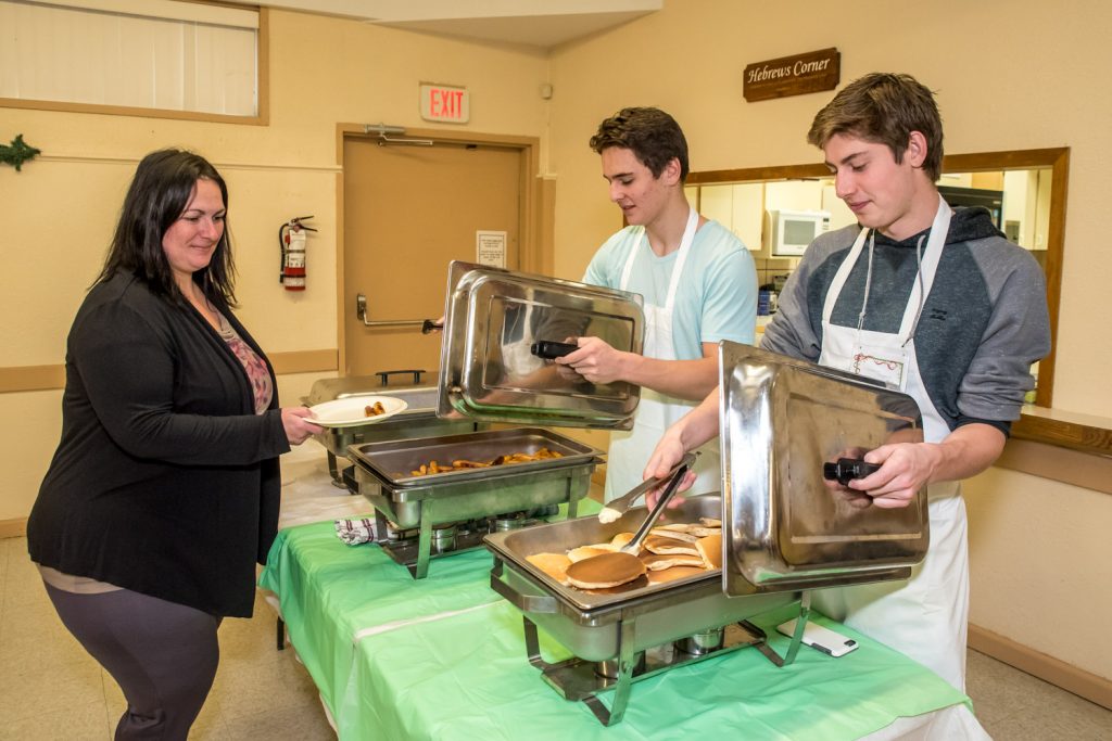 Two members of the Osoyoos Coyotes were busy serving sausages and pancakes at Breakfast with Santa and Photos Saturday morning at Osoyoos Baptist Church. Bryson Cecconi and Connor Onstein are pictured here serving Natalia Barroca. (Richard McGuire photo)