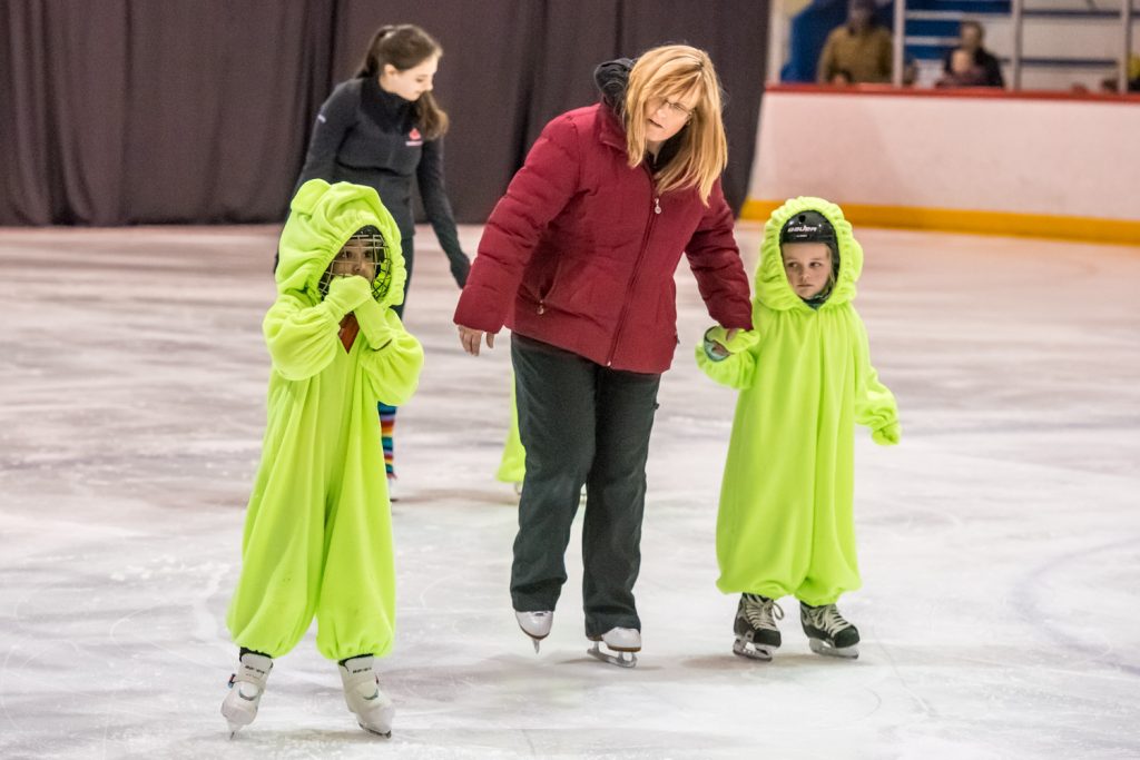 With help from Coach Andrea Umstaetter, a couple of Gummy Bears in the PreCanskate group take careful steps onto the ice. (Richard McGuire photo)