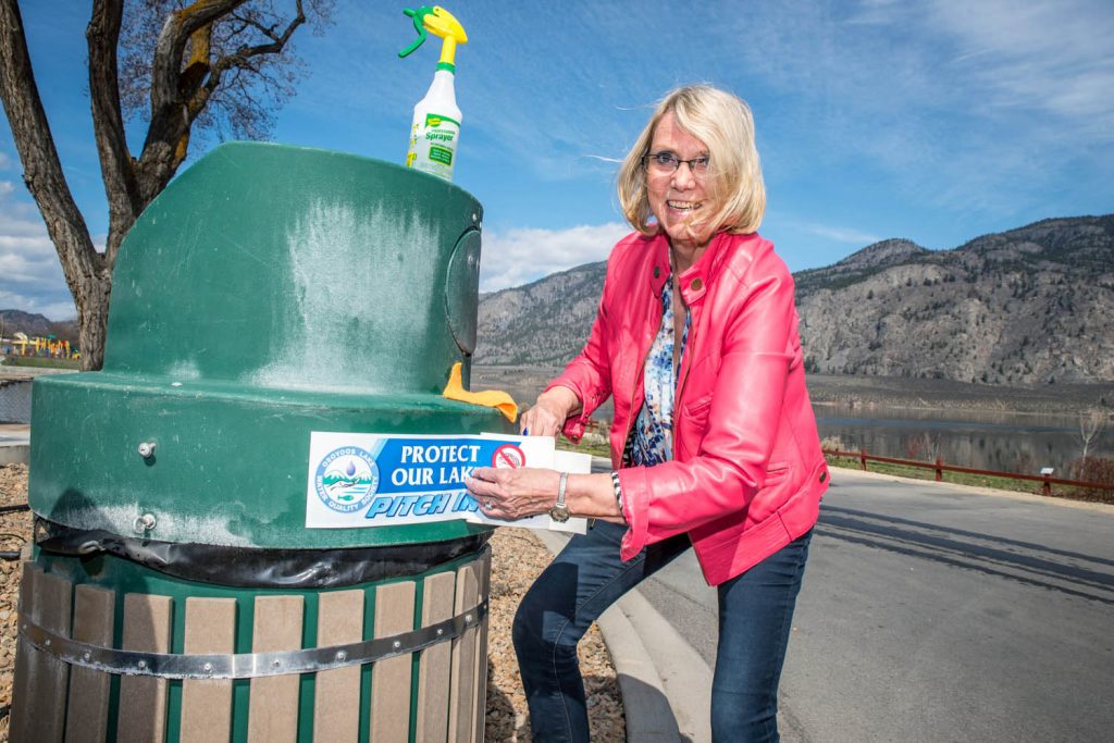 Birgit Arnstein, past president of the Osoyoos Lake Water Quality Society, organized a team of volunteers to put decals promoting the lake on trash cans along the lake's walkways on Saturday. She demonstrated the technique to volunteers, who then branched out to cover different parks and walkways. (Richard McGuire photo)