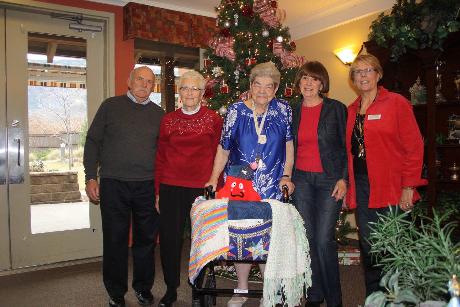Longtime Mariposa Gardens residents Marlene West and Eileen Liikala (second and third from left, respectively) have spent much of the past five years knitting, crocheting and sewing. They then sell their artwork and materials once a month and every Christmas and donate the proceeds to local charities and organizations. The two ladies estimate they’ve donated more than $5,000 over the past five years. They recently donated $600 to the breakfast programs at local schools. Joining them for the presentation were school breakfast program board treasurer Jim Harrington (far left), his wife June, who is a volunteer board member, and Louise Dawe, manager of assisted living at Mariposa Gardens. West and Liikala made all of the materials shown on Liikala’s walker. (Keith Lacey photo)