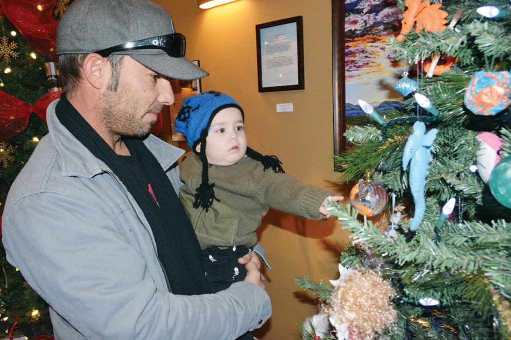 Toddler Walker Pacheco reaches for a Christmas tree ornament while checking out the Festival of Trees with dad Phil Pacheco. (Lyonel Doherty photo)