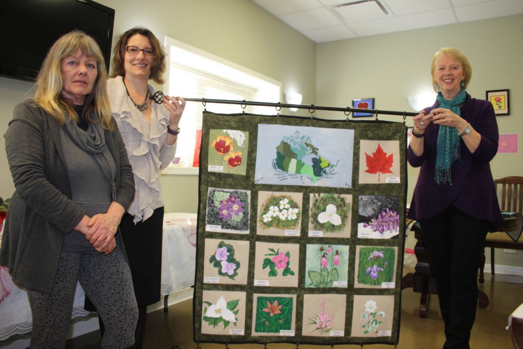 Award-winning artistic quilter Leslie Forbes (right) was invited by Gail Howard (left) to speak to the members of the Sunshine Ridge Art Group on Monday. Howard has been teaching art skills to the members for the past several months. The members made this lovely wall hanging to give to Forbes as a thank you for her presentation to them. Also seen is Sunshine Ridge manager Tracy Harfman. (Keith Lacey photo)