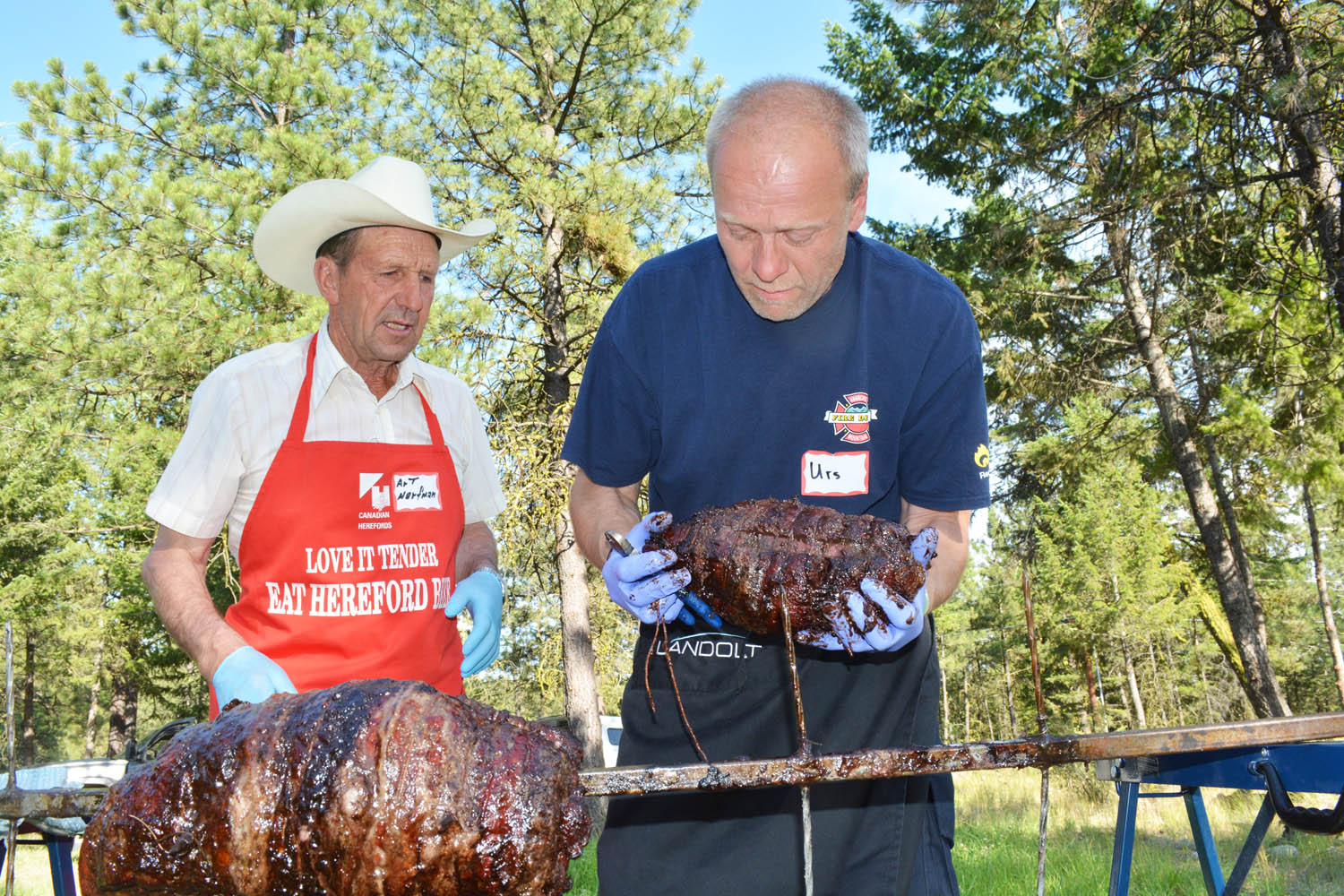 Chief cook Art Harfman (left) watches closely as firefighter Urs Grob takes the beef off the spit during the annual barbecue hosted by the Anarchist Mountain Fire Department at the Summit Centre on July 12. (Lyonel Doherty photo)