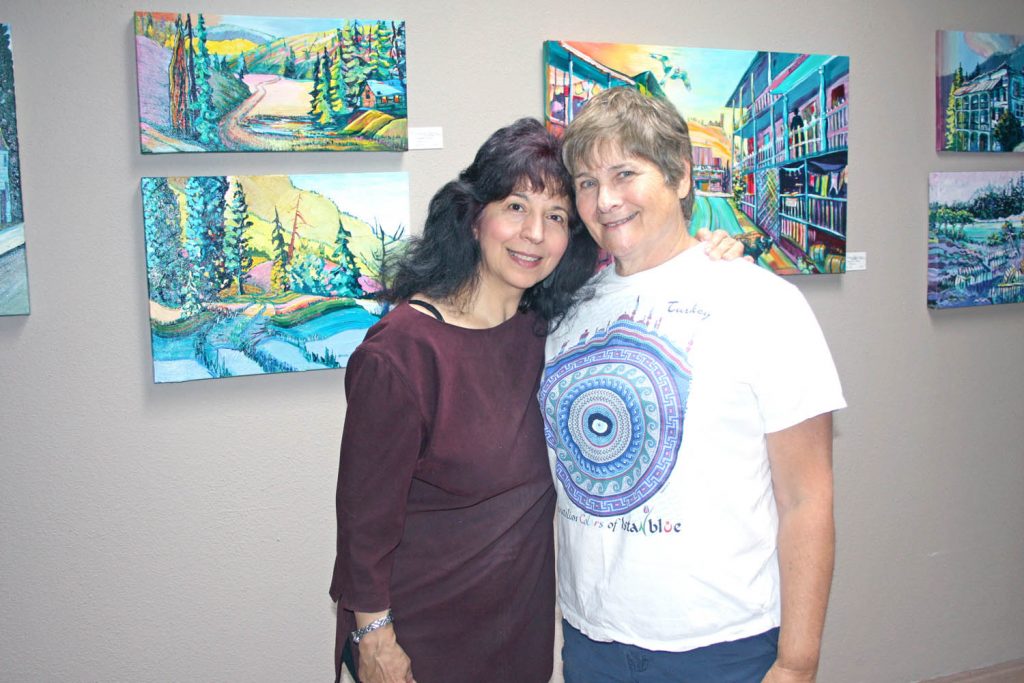 Sandra Albo (right), the vice-president of the new Okanagan Art Gallery, formerly the Oliver Art Gallery, stands in front of several of her colourful paintings, with good friend and fellow artist Carmen Tome. The Okanagan Art Gallery opened for business at its new location on Main Street in Osoyoos on Tuesday morning. (Keith Lacey photo)