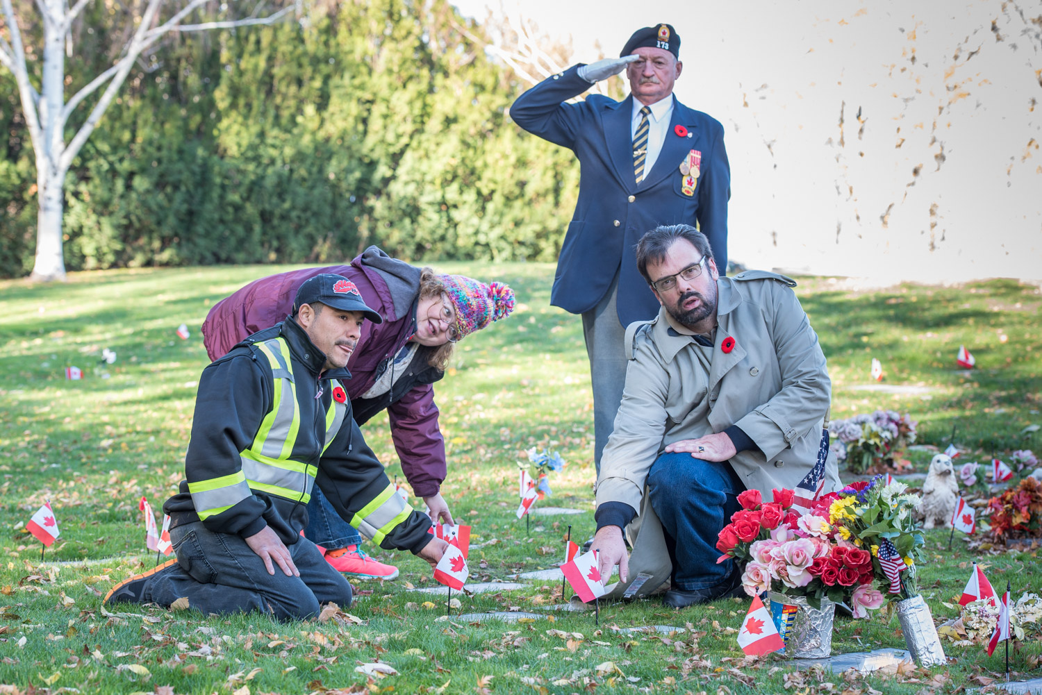 Three Osoyoos members of the Kiwanis Aktion Club placed flags beside the grave markers of veterans at Lakeview Cemetery on Osoyoos on Monday. The club is for adults with disabilities, primarily learning disabilities. From left are Alberto Holz, Angela Flannigan and Warren Scherk. In the background saluting is Gary Fox, representing the Royal Canadian Legion. (Richard McGuire photo)