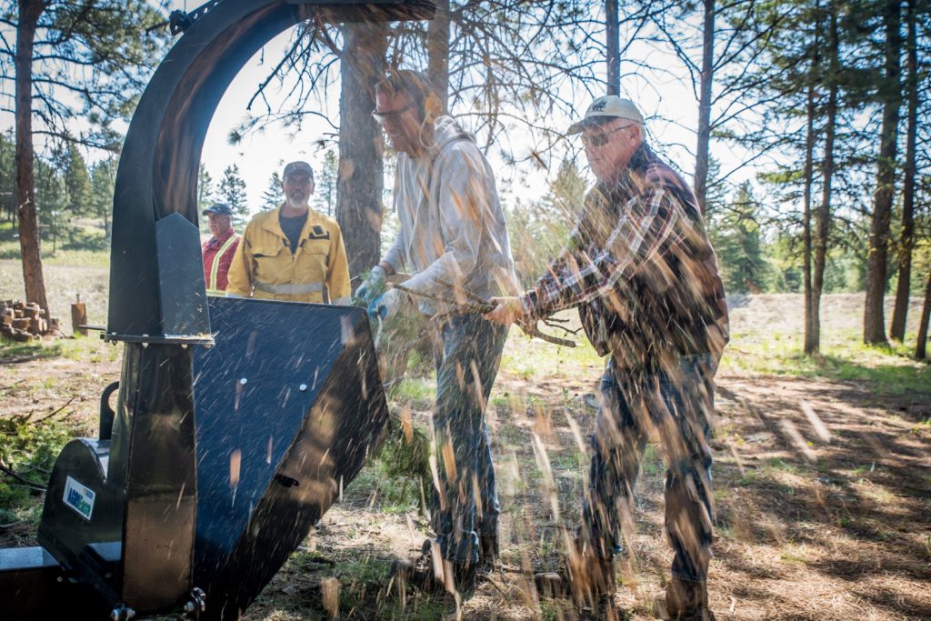Brent Gilbey and Darrell Latimer feed a wood chipper with branches in a community effort to reduce fire hazards. Behind and helping (left) was Gerrit Nienhuis. Members of the Anarchist Mountain Community held an event on Saturday for National FireSmart Preparedness Day. Many volunteers turned up on the sunny day to clean up brush and other fire hazards at Sasquatch Pond Park. Anarchist Mountain is one of the few communities in B.C. to achieve FireSmart status as a result of its citizen program to reduce the risk of fire damage. (Richard McGuire photo)