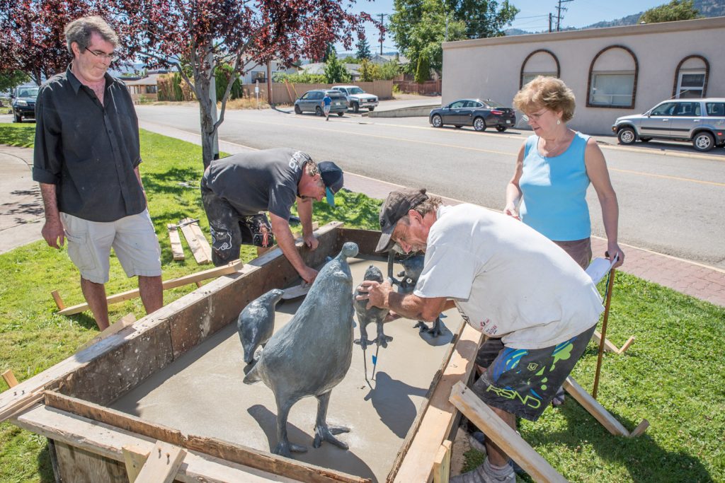 Artists Peter Scott (left) and Deb Sherwin (right) direct the placement of the new quail sculptures in front of the Osoyoos Art Gallery, while Rick Holz (second from left) smooths out some concrete and Kirk Hood (second from right) places one of the baby quails. Holz and Hood are from CSI Contract, one of the companies contributing to the project. (Richard McGuire photo)