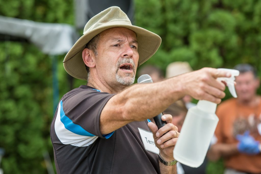 With a microphone in one hand and a water bottle to spritz hot migrants in the other, Senior Pastor Terry Kaethler delivers a message about Jesus before the meal. Kaethler is from Mountain Park Community Church in Abbotsford, which partners with Osoyoos Baptist Church to bring meals to the migrants. (Richard McGuire photo)