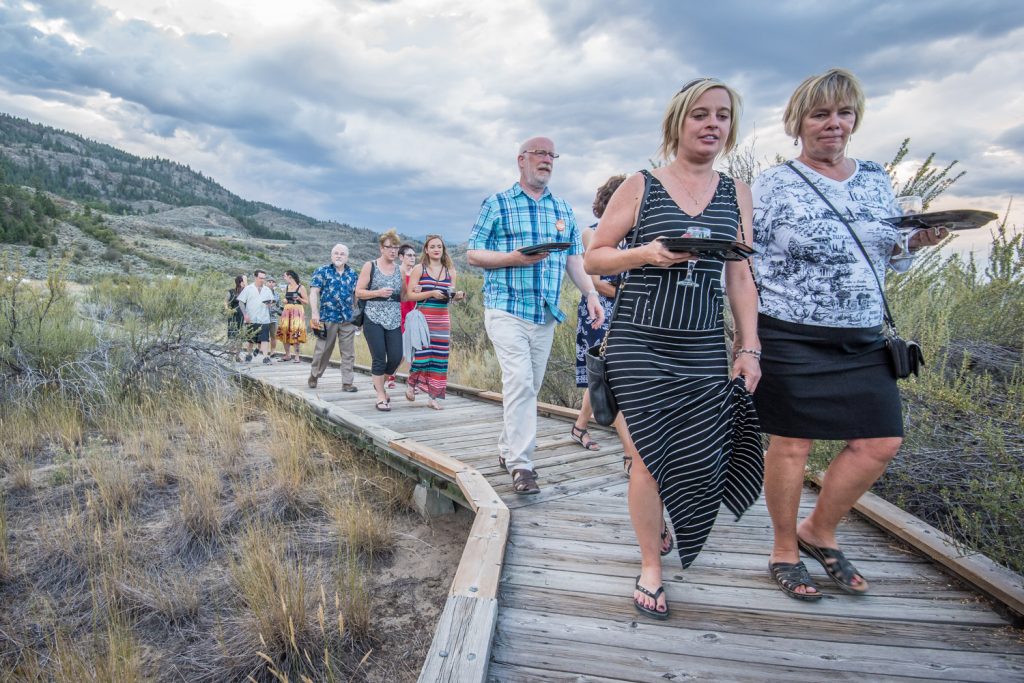 Guests carry plates and wine glasses on a tour of the boardwalk at Romancing the Desert. At various stops along the way they had a chance to sample wine and desserts. (Richard McGuire photo)