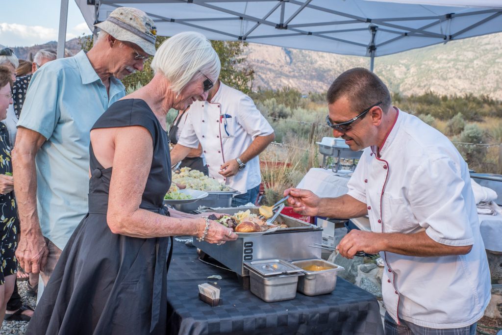 Erhard Ridener (right) adds a dab of mustard to a guest's plate after serving roast pork for Crowsnest Vineyards Restaurant at Romancing the Desert Saturday evening at the Osoyoos Desert Centre. (Richard McGuire photo)