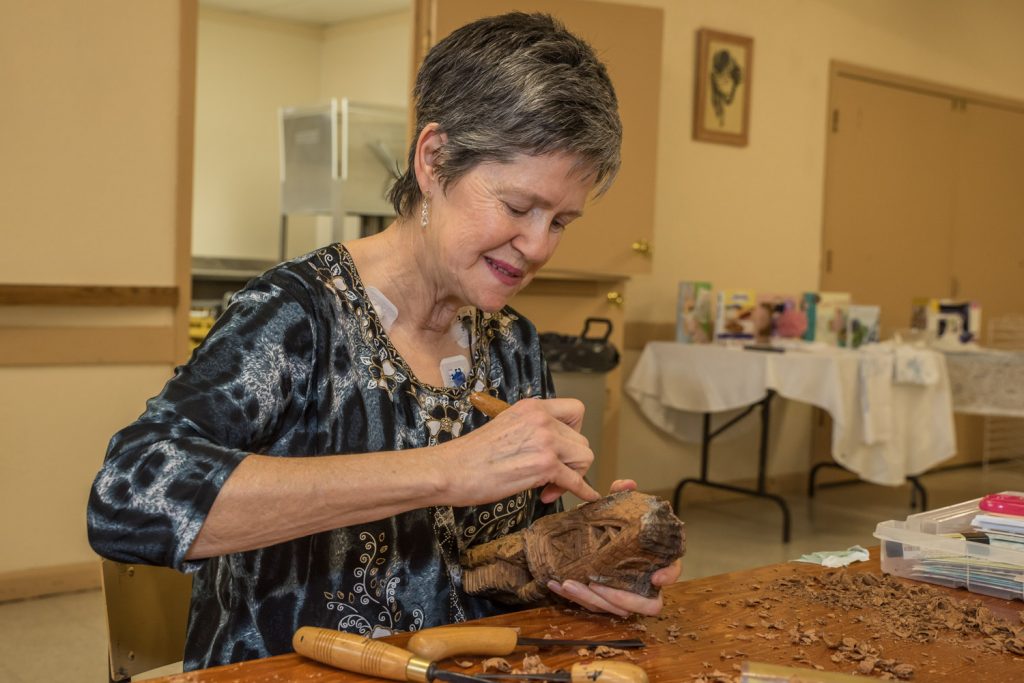 Helen Maw, a snowbird from Edmonton staying at Nk'Mip Campground, worked on making woodcarvings at the Osoyoos Baptist Church on Saturday. Participants rented tables to do their work as a fundraiser for Desert Sun Counselling's Men's Counselling Program. Maw's intricate carvings of figures are done in cottonwood bark. (Richard McGuire photo)