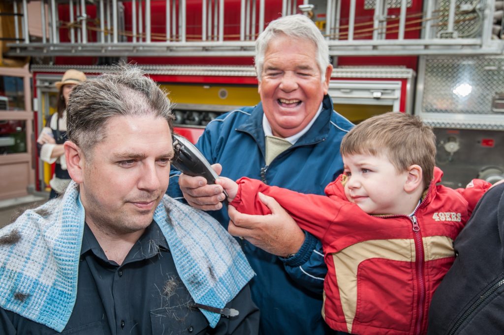 Osoyoos firefighter Chris Parker (left) gets his hair shaved by his son, Adam. Ray Parker (back), Chris's father and Adam's grandfather, gave the little one a bit of help. The firefighters allowed their heads to be shaved to raise money for cancer. (Richard McGuire photo)