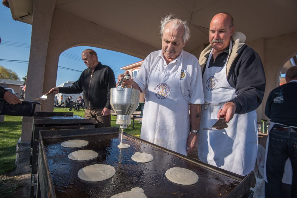 Jim King, a Rotarian and town councillor, releases pancake batter onto the grill as Blake Somerset (right) stands by to flip them. The Rotary Club of Osoyoos took over the pancake breakfast  after the Lions Club disbanded last year. In the background, Garnet Tarr scoops pancakes into a pan. (Richard McGuire photo)