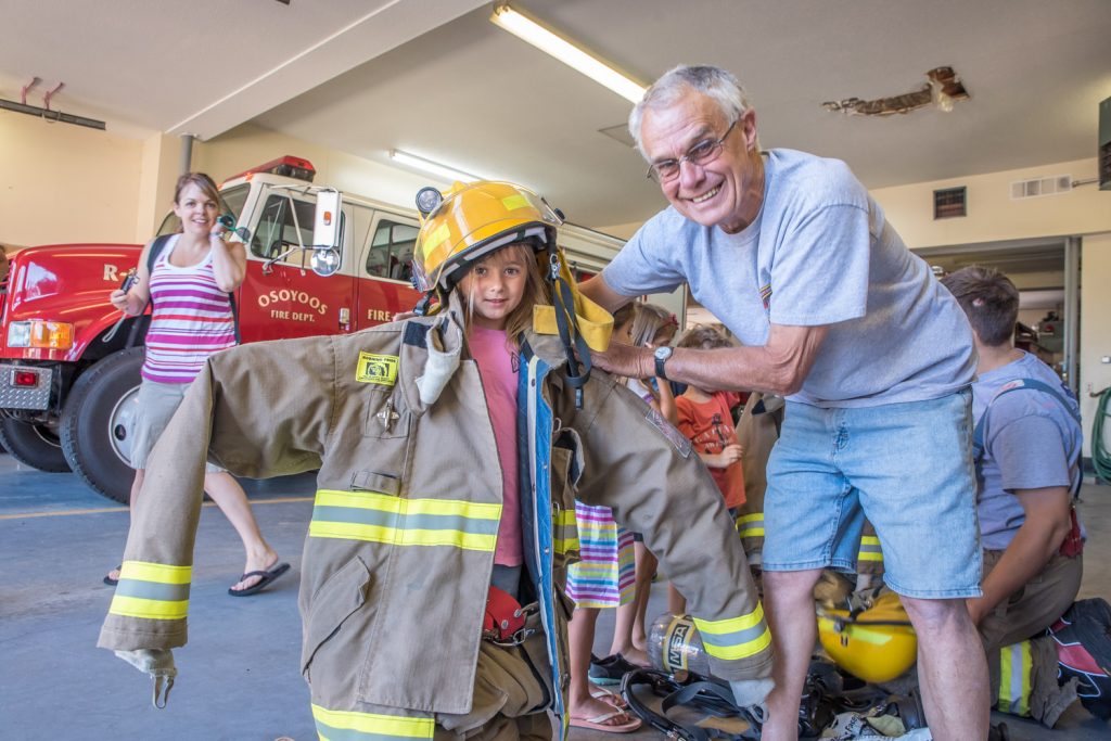 Kendall Mullen-Knight gets decked out in firefighting gear with a little help from Osoyoos firefighter Ross Driver. The Kindergarten student and her Osoyoos Secondary School classmates took a field trip to the firehall last Wednesday. (Richard McGuire photo)