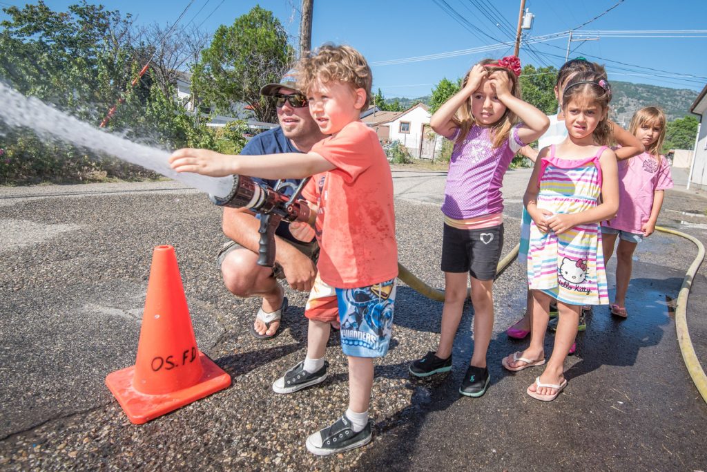 With a little guidance from Osoyoos firefighter Todd Kunz (left), Chase Salmond aims a fire hose. Watching and awaiting their turn are Sophia Pollard, Miley Rahmanian and Kendal Mullen-Knight. (Richard McGuire photo)
