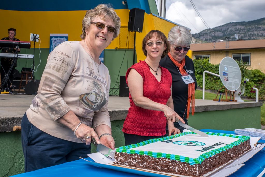 Judy Dallas (left) and Alicia Osland prepare to cut a cake celebrating the 25th anniversary of the Osoyoos Lake Water Quality Society. Ambassador Gloria Ellingson looks on, preparing to help serve. Dallas is the wife of the late OLWQS pioneer Lional Dallas and Osland was involved with the society for many years. (Richard McGuire photo)