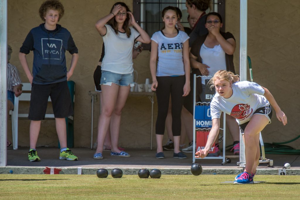 Amy Kneller tries lawn bowling for the first time at an event last week for seasonal employees of Watermark Beach Resort. At right, Naga Terada, president of the Osoyoos Lawn Bowling Club, gave the newbie lawn bowlers pointers on technique. Watching from behind is Irene Harfman, from Osoyoos, who has also been working at Watermark. Some of the newbies said the sport reminds them of bocce, although the rules are more similar to curling. The Osoyoos Lawn Bowling Club has been doing outreach to try to involve younger participants in the sport. (Richard McGuire photo)