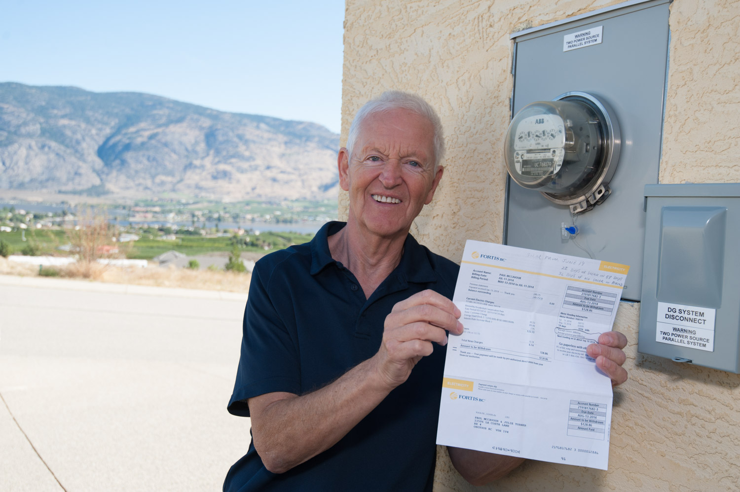 Paul McCavour shows his FortisBC power bill that is greatly reduced from this time last year, even though his solar panels were only operating for a small part of the billing cycle. Beside him, his power meter is running backwards thanks to the solar power being produced by 24 panels on the hill above his home. McCavour hopes the price of large capacity batteries continues to fall so that he will be able to store power for use at night and other times when the sun isn't strong enough. (Richard McGuire photo)