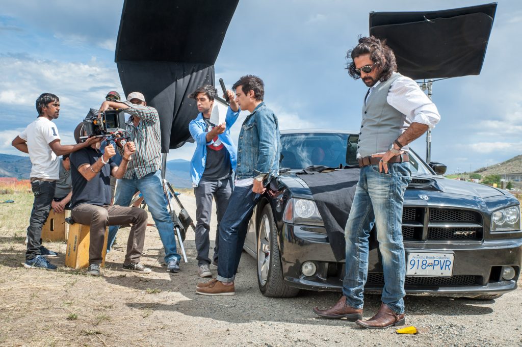 Director Baljit Singh Deo (seated) looks at the scene as crew and actors Jimmy Shergill (leaning on car) and Mukul Dev (right) prepare for take 2. They were filming a scene for the Punjabi movie Crash at the airport in Osoyoos. (Richard McGuire photo)
