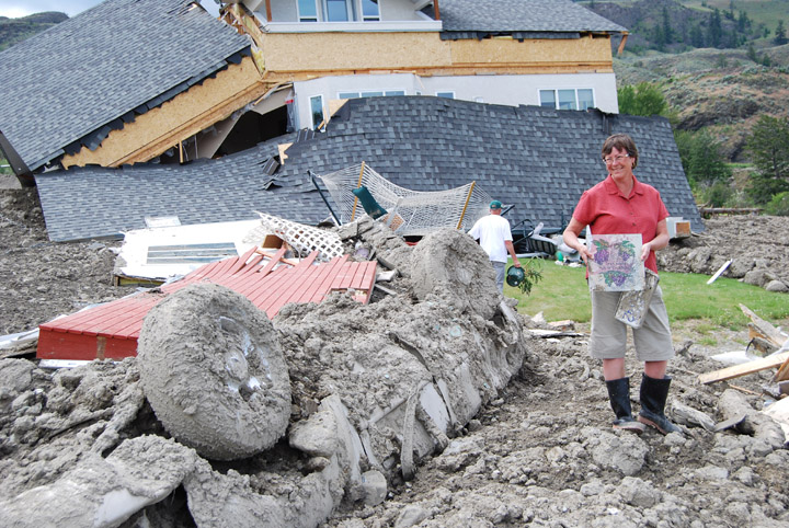mudslidefoloweb Rural Oliver resident Kathy Mercier stands among the chaos left in the wake of a massive mudslide on June 13. She is standing next to her 2005 Ford Explorer Sport Trac – upside down and in the mud – and holding a sign that used to advertise the “Grapevine Bed and Breakfast” which she and her husband owned. Photo by Laurena Weninger - Click on picture for larger image