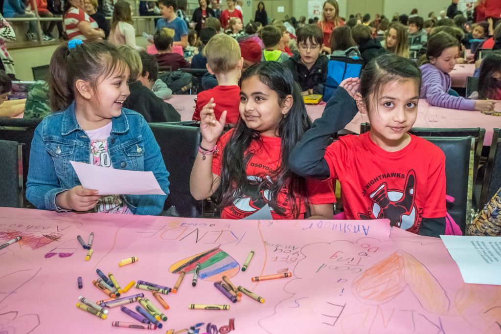 Students draw with crayons on pink paper table coverings at a school rally to conclude 21 Days of Kindness. The pink symbolizes anti-bullying. From left are Riya Sandhu, Anshnoon Mann and Riya Brar. (Richard McGuire photo)