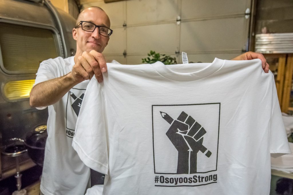 Jamie Elder, owner of Unity Osoyoos, shows one of the T-shirts he's making with the hashtag #OsoyoosStrong. These will be given out this week to students at Osoyoos Secondary School and will be sold in the community for a minimum donation of $20. Money raised will go to support a new independent school in Osoyoos. (Richard McGuire photo)