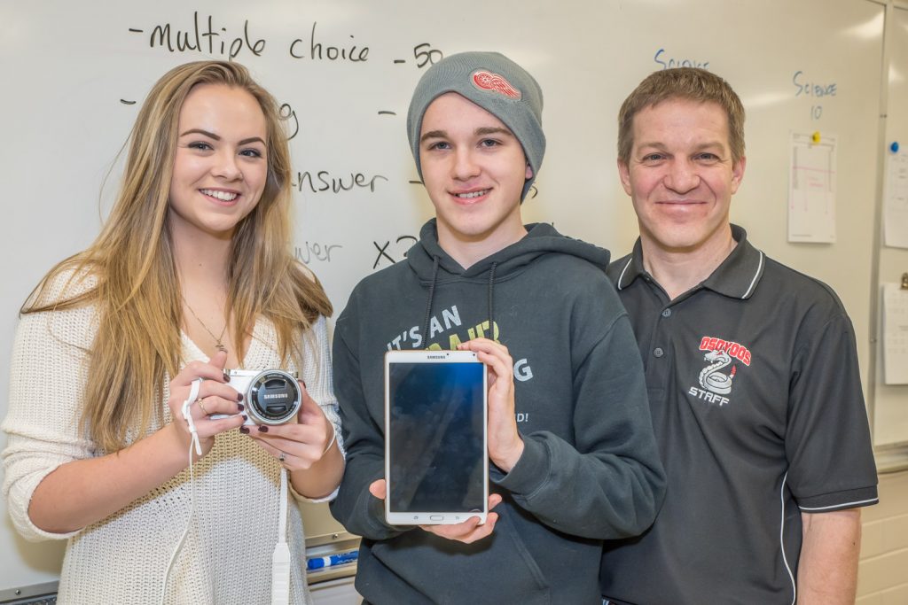 Students Taylor Price and Adair Langsmith, both in Grade 11 at Osoyoos Secondary School (OSS), show off a camera and tablet the school received from Samsumg for placing as semi-finalists in the Samsung Solve for Tomorrow Challenge. OSS was one of 55 semi-finalists chosen across Canada, based on a proposal put forward by teacher Peter Gajda, right. The students will look into ideas the Town of Osoyoos can use to conserve water. (Richard McGuire photo)