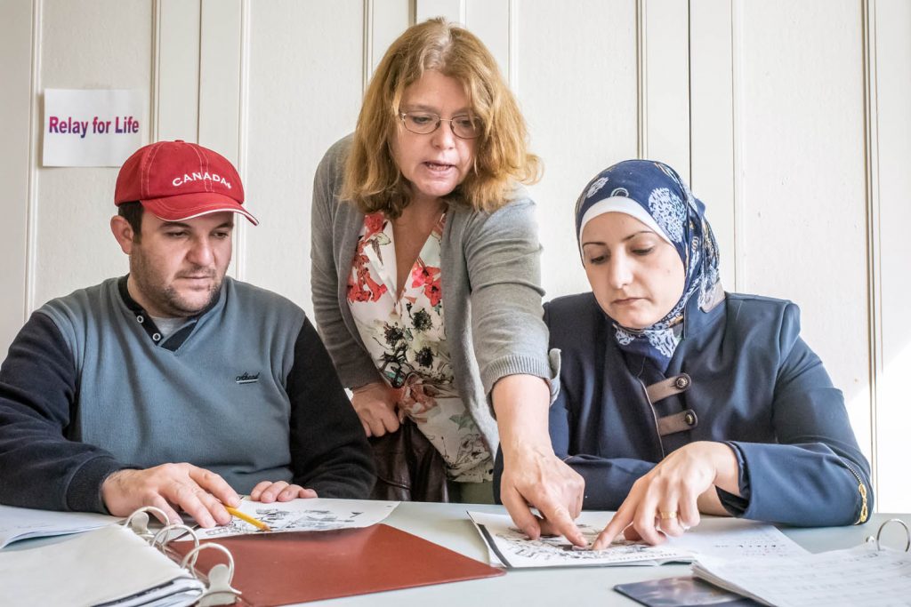 Teacher Wendy Neumann (centre) gives Mohamad and Aya a two-hour English lesson at the Sonora Centre. Here they learn the English words for items in illustrations. (Richard McGuire photo)