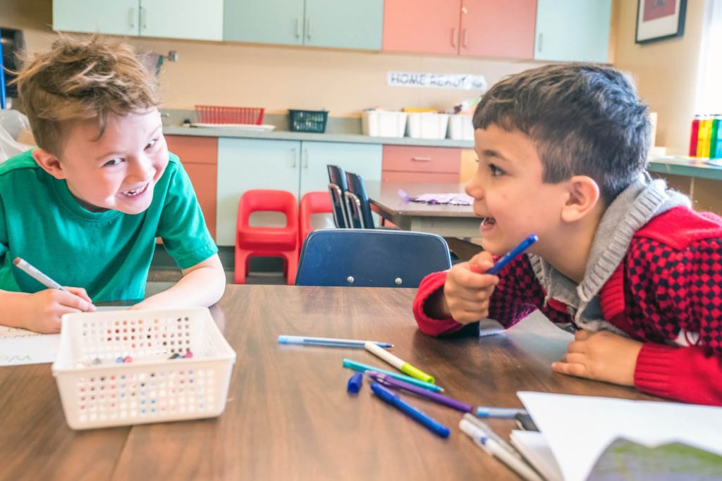 Despite language challenges, Samer, right, shares a laugh with fellow Kindergarten student Grayson Stevenot as the two draw pictures in their booklets. (Richard McGuire photo)