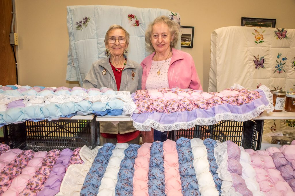 Margaret Rosenberg, left, of Okanagan Falls, and Heather Leslie, of Oliver, showed off handmade quilts, preserves and baking at their booth at the Christmas Craft Fair on Sunday organized by Osoyoos Royal Purple at the Elks Hall. According to these ladies, Leslie makes everything while Rosenberg excels in selling and consuming it. The fair had craft booths on both the main and lower floors and it was well attended. (Richard McGuire photo)