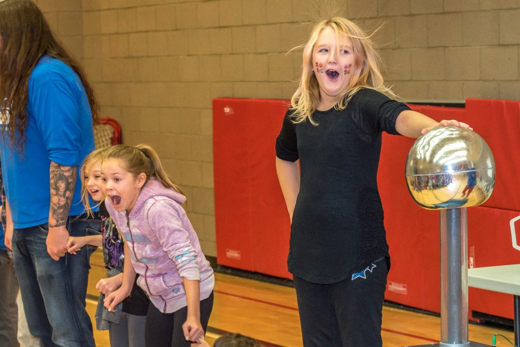 Hair rises on Emma Palmateer's head as she touches a Van de Graaf generator, which produces a low-voltage electric current. She's just sent a shock down a chain of students with linked arms. Alesia Dortman and Paige Hanson react to their shocks. (Richard McGuire photo)