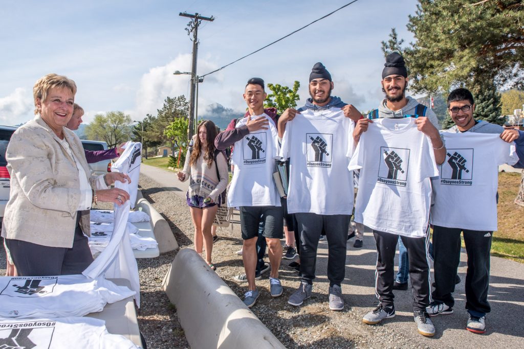 Osoyoos realtor Eileen McGinn was among the volunteers handing out T-shirts to students at Osoyoos Secondary School (OSS) Friday morning with the hashtag #OsoyoosStrong. The shirts were created by Jamie Elder of Unity Osoyoos, along with other volunteers. They are intended to show pride for education in Osoyoos. Proceeds raised from selling the shirts in the community will help to fund an independent community high school, which many in the community hope will fill the void left by the planned closure of OSS. (Richard McGuire photo)