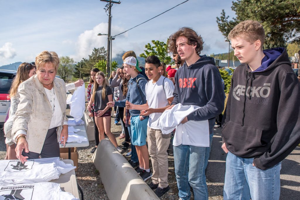 Osoyoos realtor Eileen McGinn was among the volunteers handing out T-shirts to students at Osoyoos Secondary School (OSS) Friday morning with the hashtag #OsoyoosStrong. The shirts were created by Jamie Elder of Unity Osoyoos, along with other volunteers. They are intended to show pride for education in Osoyoos. Proceeds raised from selling the shirts in the community will help to fund an independent community high school, which many in the community hope will fill the void left by the planned closure of OSS. (Richard McGuire photo)