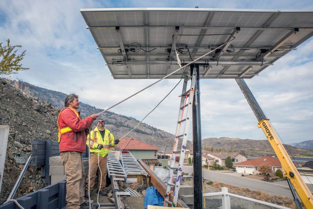 Roger Huber (left) and Richard Steuble of Swiss Solar Tech position solar panels on a pole behind Paul McCavour’s house. There McCavour will be able to angle them according to the season to capture the most sunlight. The panels were previously on the ground where they were often shaded after 2 p.m. McCavour preaches the merits of solar power to reduce electricity bills over the longer term and contribute to a greener planet. (Richard McGuire photo)